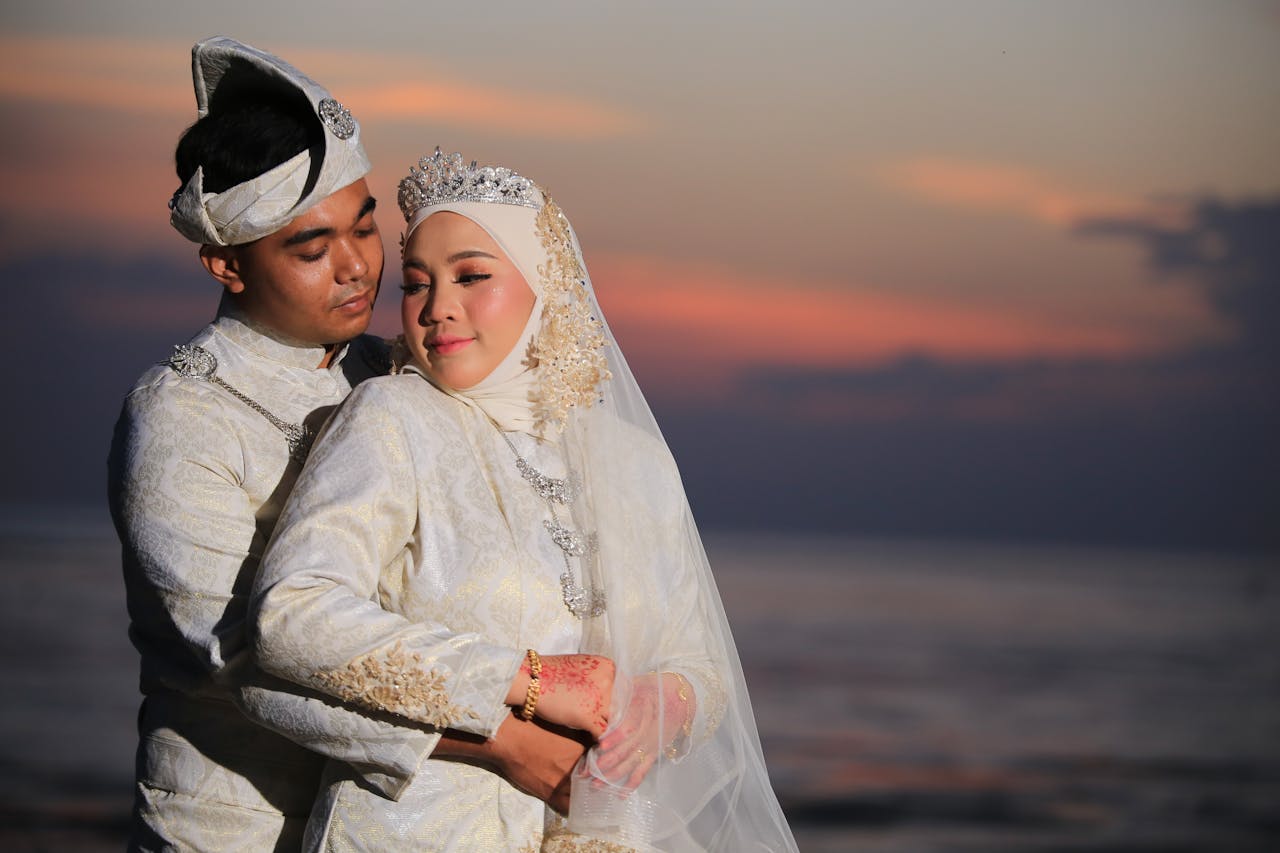 get-in-touch An Asian couple in traditional wedding attire shares a loving embrace at sunset by the sea.