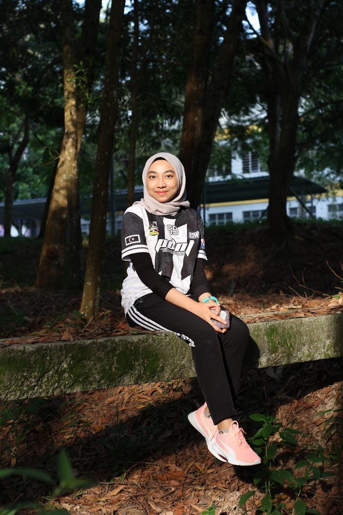 services-06 A young woman in a headscarf smiles while sitting in a sunlit forest in Tapah, Malaysia.