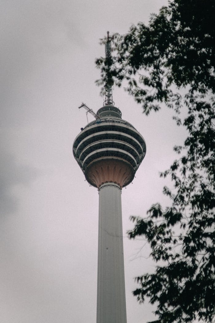 why-choose-us A view of the iconic KL Tower in Kuala Lumpur, framed by trees against a cloudy sky.