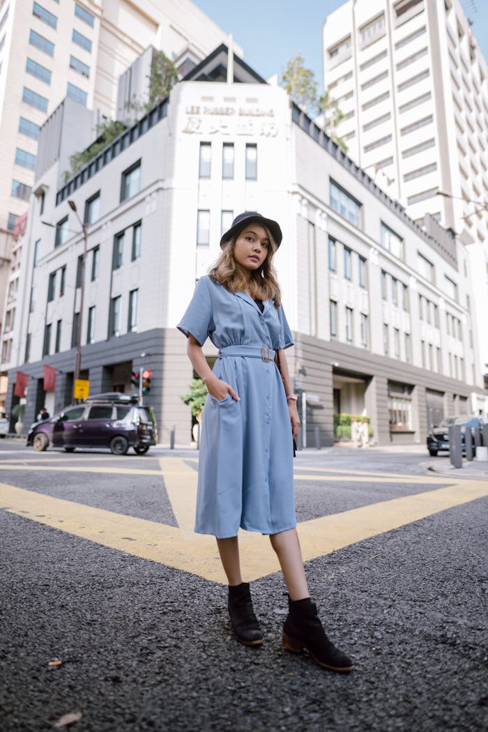 Fashionable woman in blue dress poses on a Kuala Lumpur city street against modern architecture.