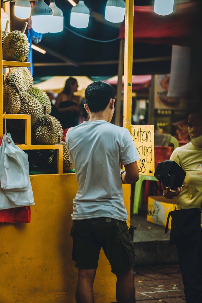 A vibrant scene at a street market in Kuala Lumpur with people and fruit stalls.