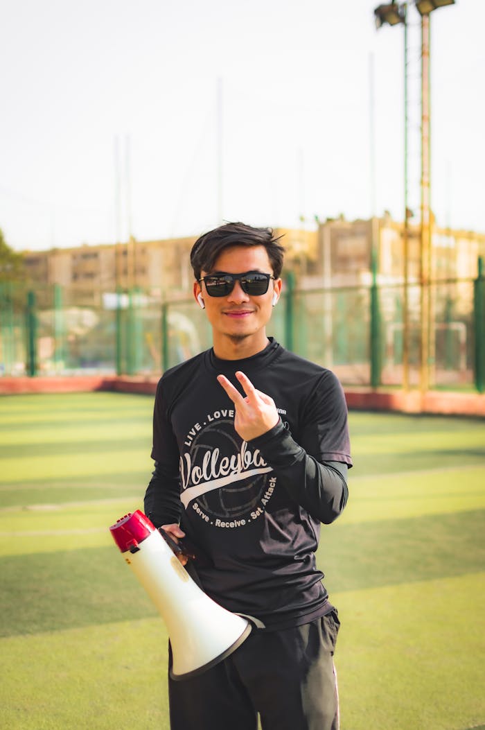about-us Casual portrait of a young man outdoors holding a megaphone and showing a peace sign, smiling with sunglasses.